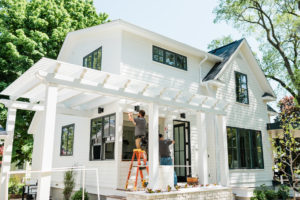 A beautiful home with white siding has a white pergola installed on the exterior.