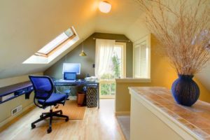 Skylight allows light to shine into an attic office space featuring a blue chair